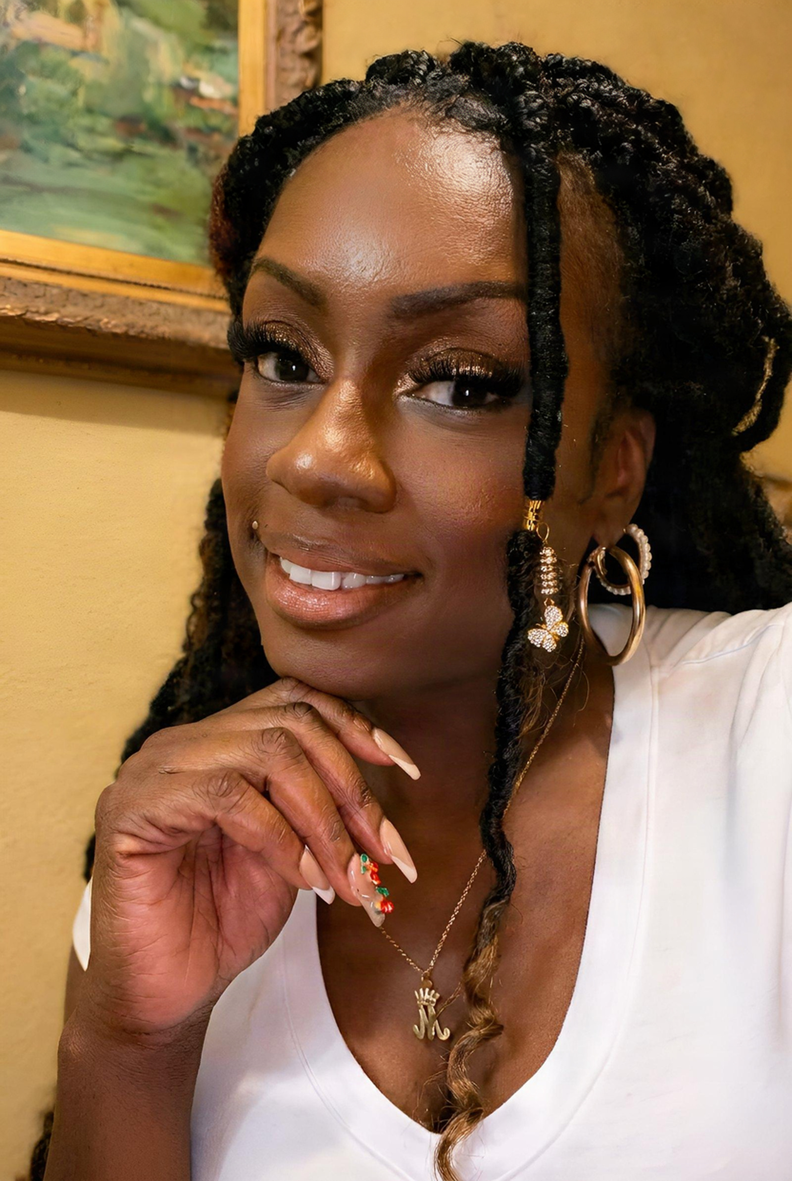 Janay Lewis smiling, hand at her chin, in a white top with gold hoops