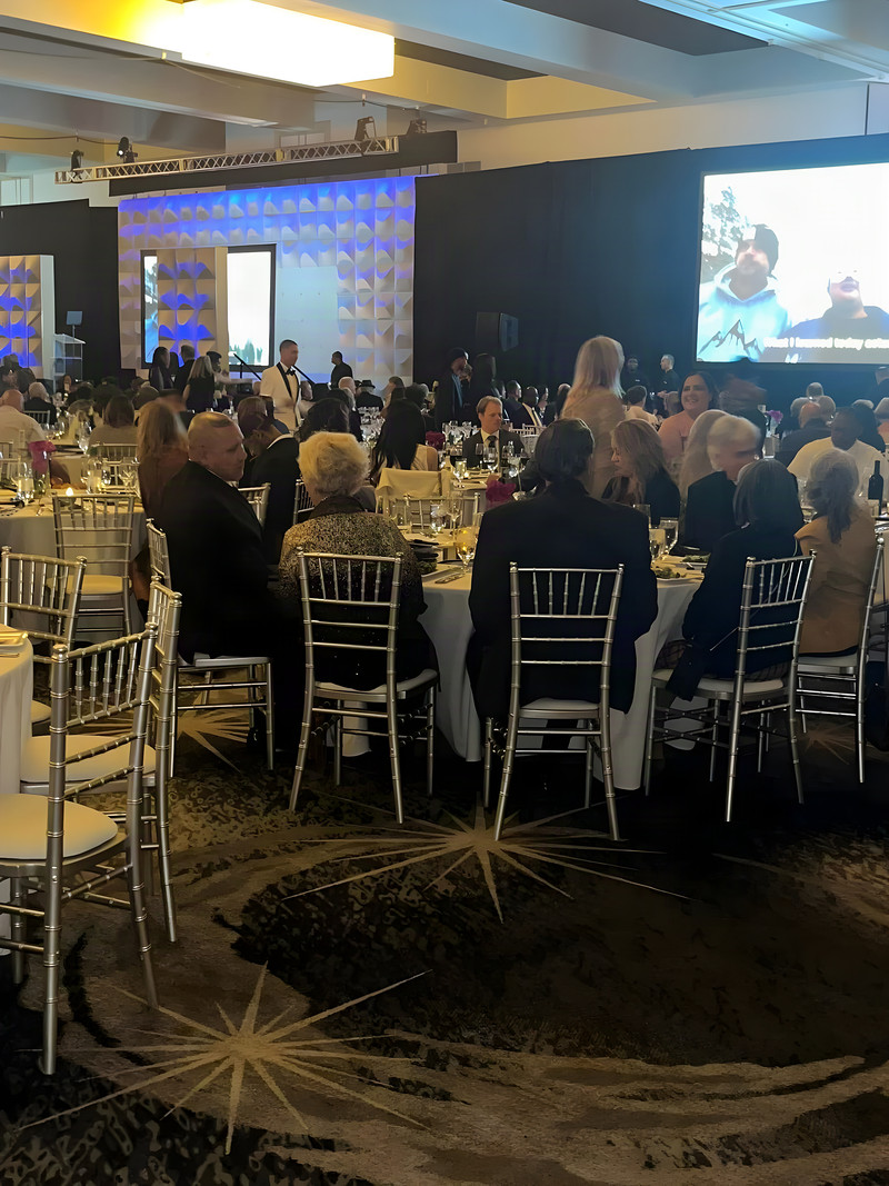 Formal gala ballroom with round tables, silver chairs and a stage screen